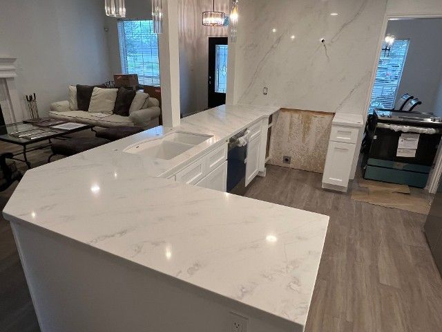Modern kitchen with white marble counters, wood floors, and a living area with a gray sofa in the background