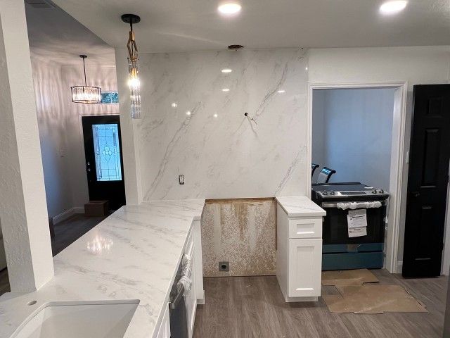 Modern kitchen with marble countertops, white cabinets, pendant lights, and a dark doorway to the right