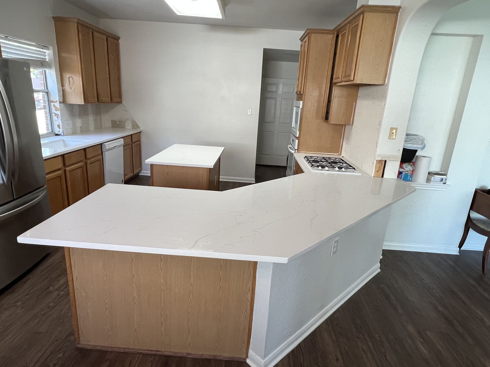 Empty kitchen with white countertops, wood cabinets, and dark flooring.