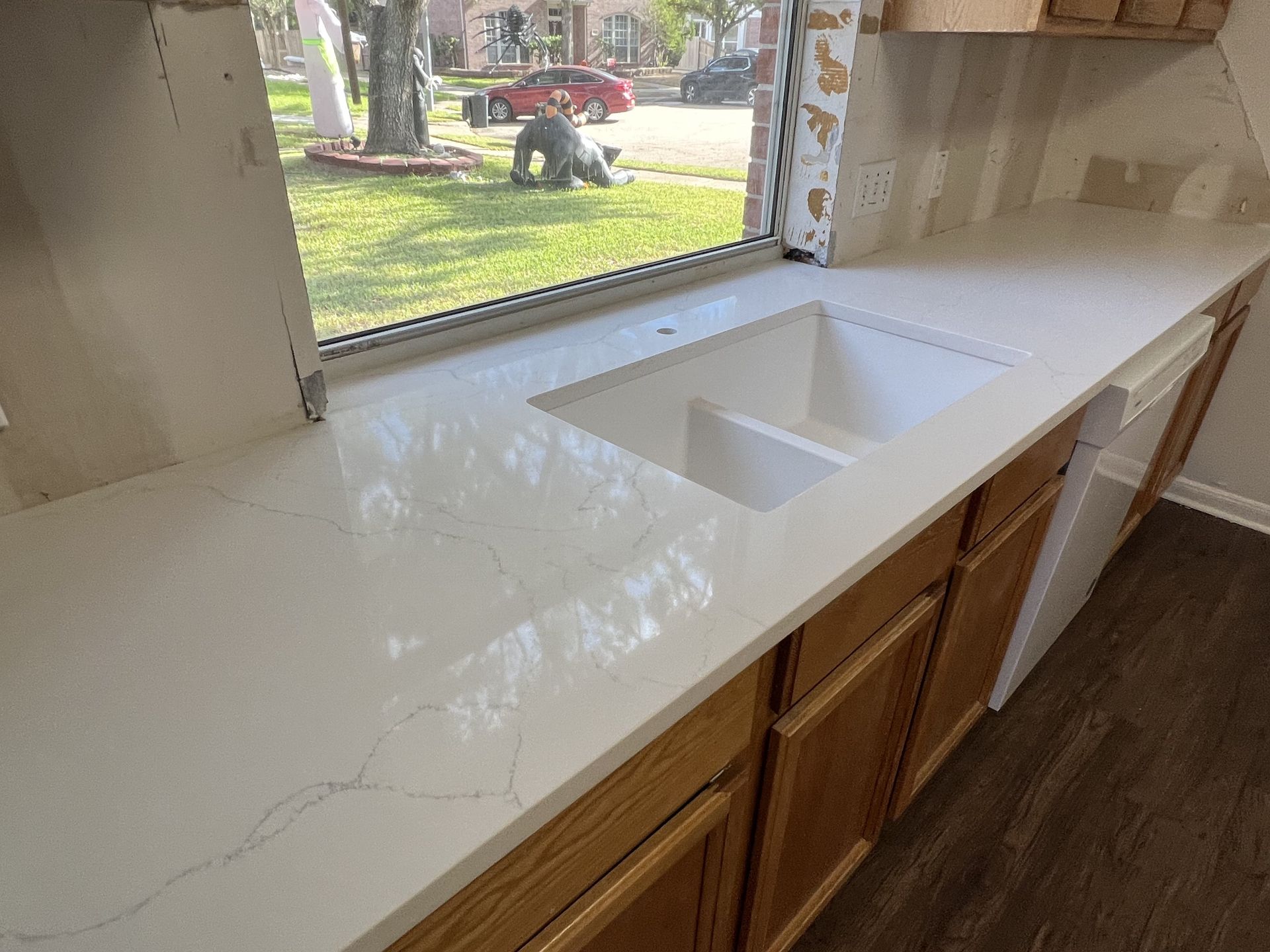 White kitchen countertop with a double sink beneath a large window overlooking a yard