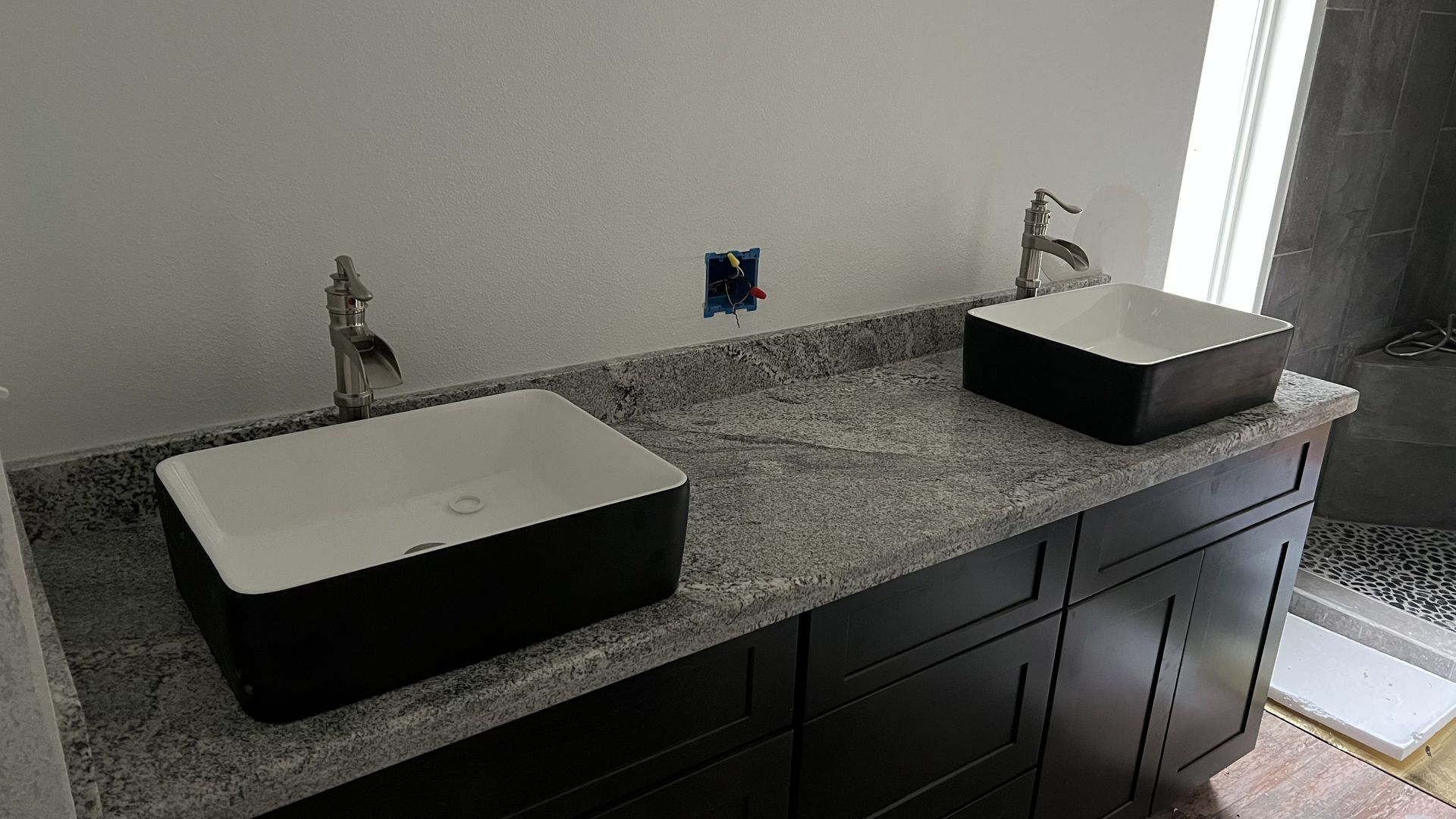 Double sink bathroom vanity with dark cabinets and light countertops beside a shower.
