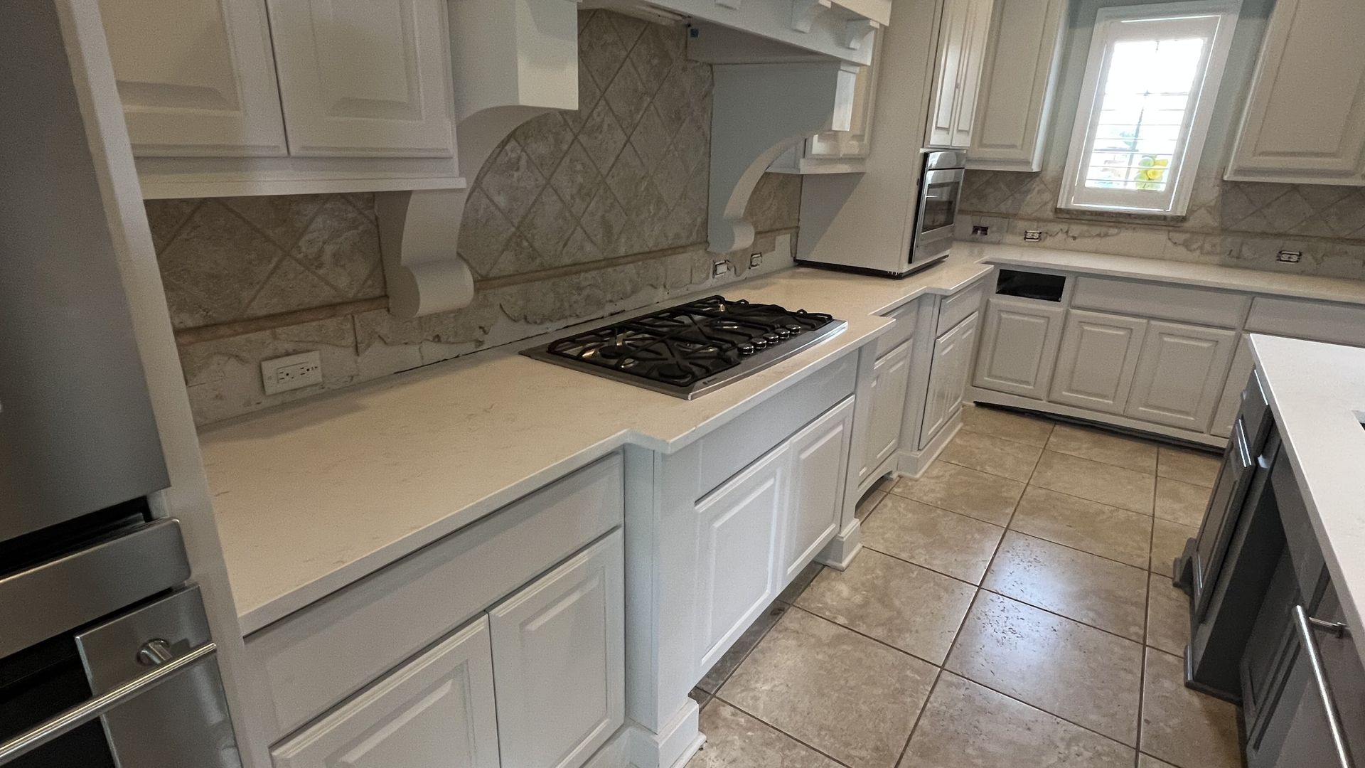 Bright modern kitchen with white cabinets, beige countertops, stainless appliances, and tiled floor.
