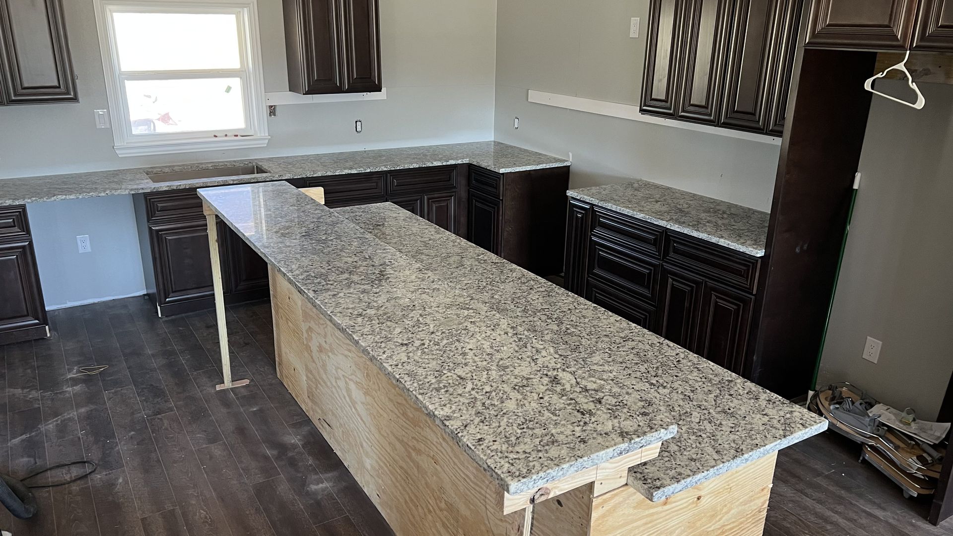 Empty kitchen with granite island, dark wood cabinets, and windows with blinds.