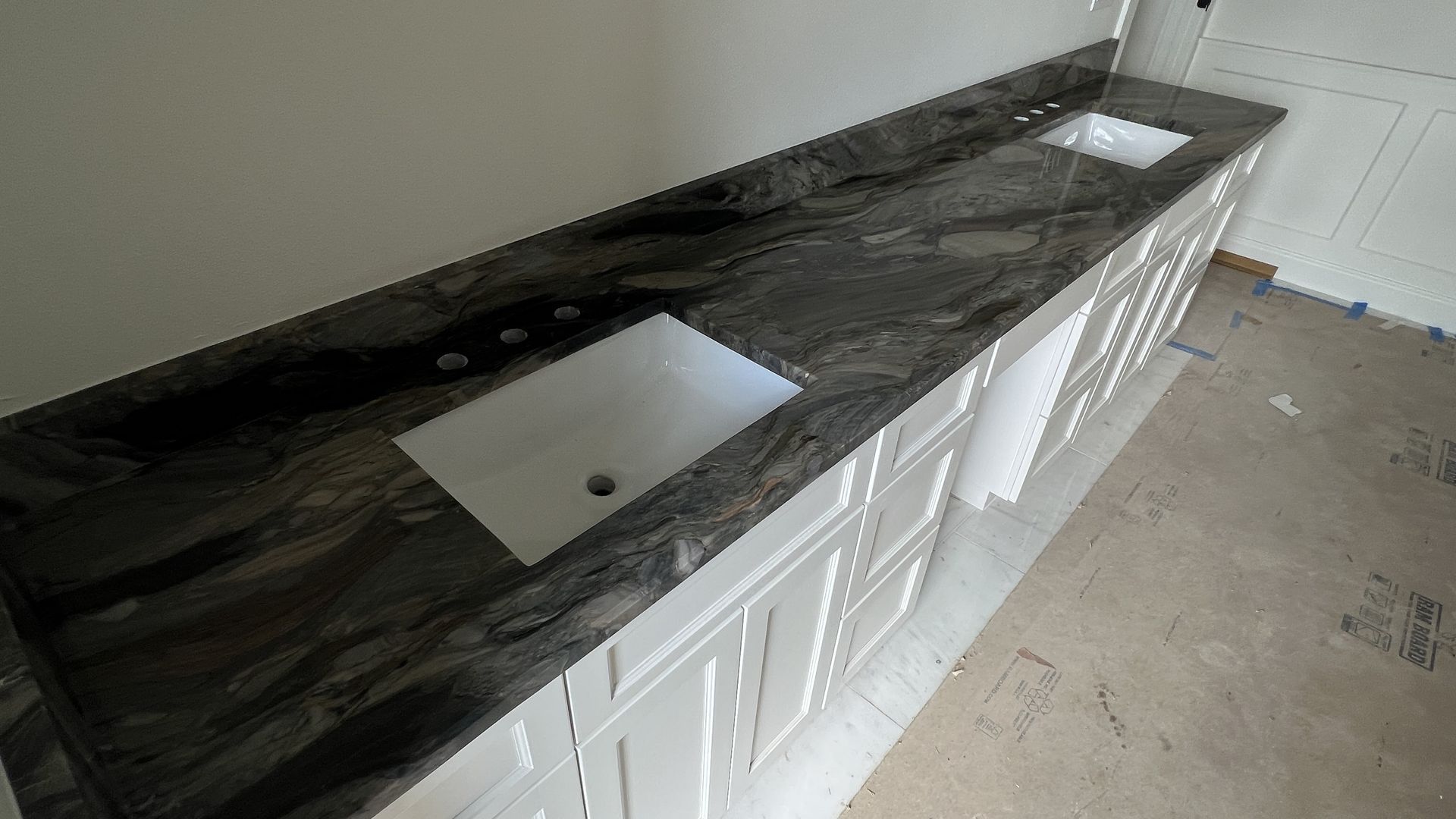 Long dark kitchen countertop with a stainless sink and white cabinets below in an unfinished room