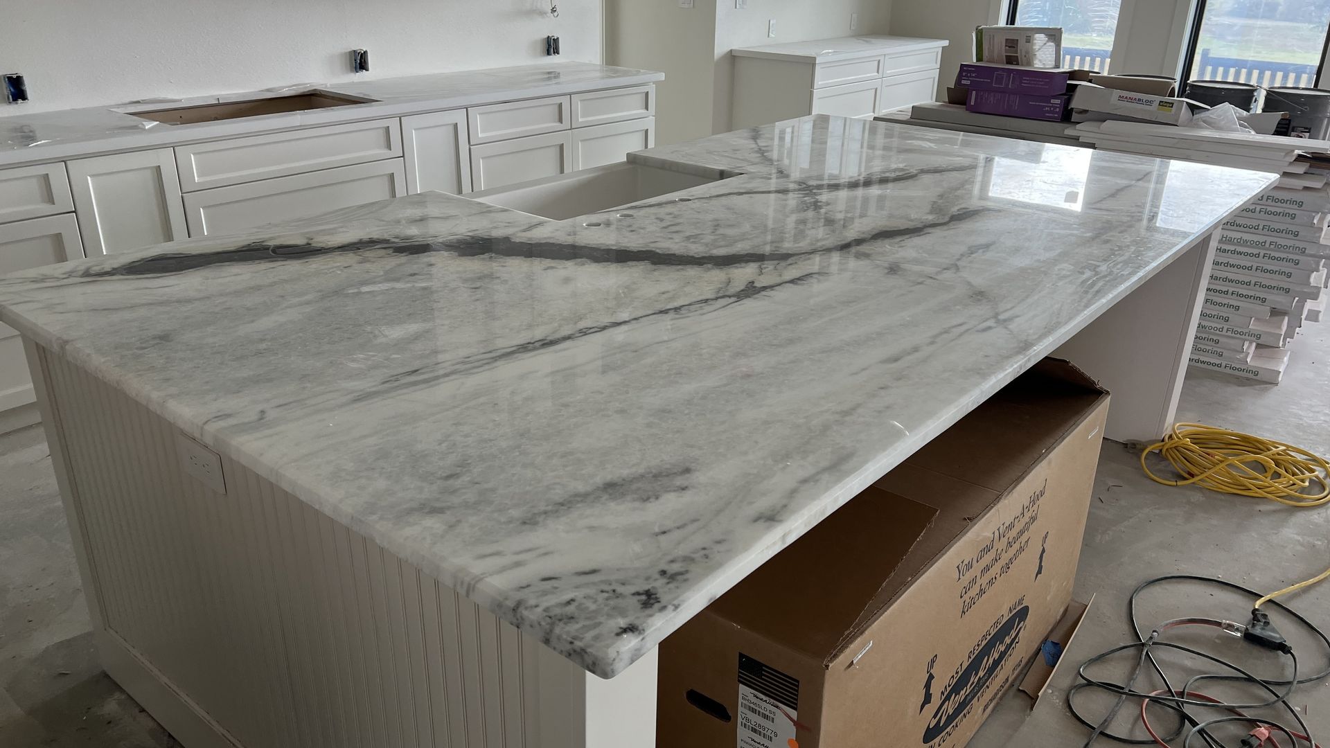 Large marble kitchen island countertop under installation in a bright, unfinished kitchen.