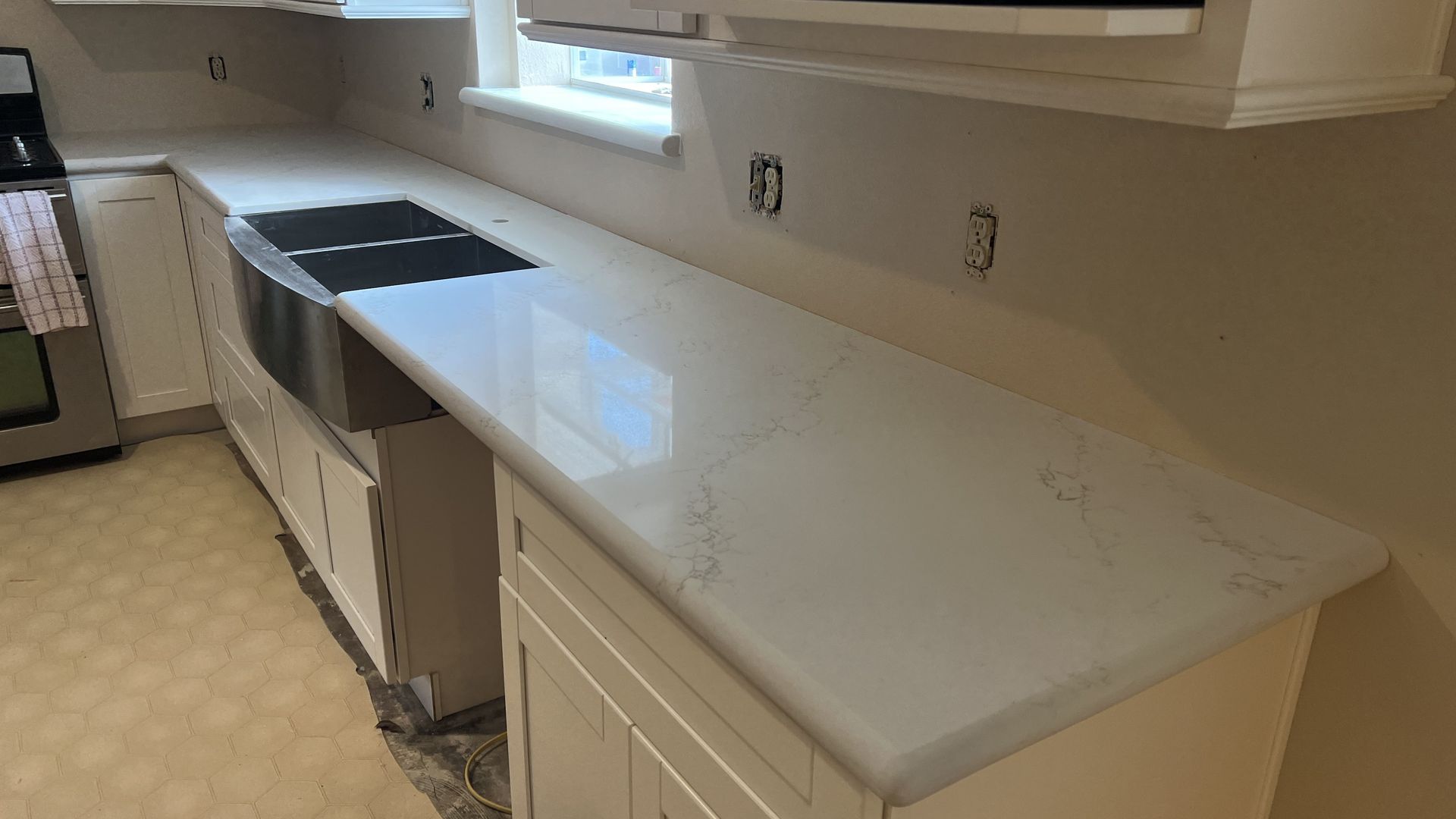 Empty kitchen countertop with white cabinets, sink, and black stovetop by a window