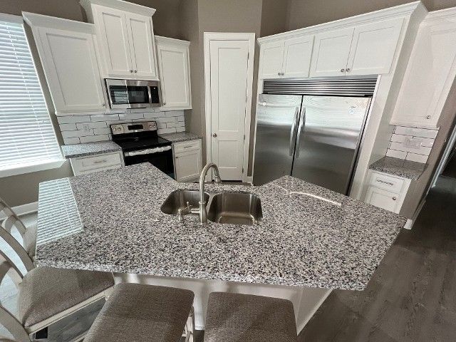 Bright modern kitchen with white cabinets, stainless steel appliances, and a large speckled island sink.