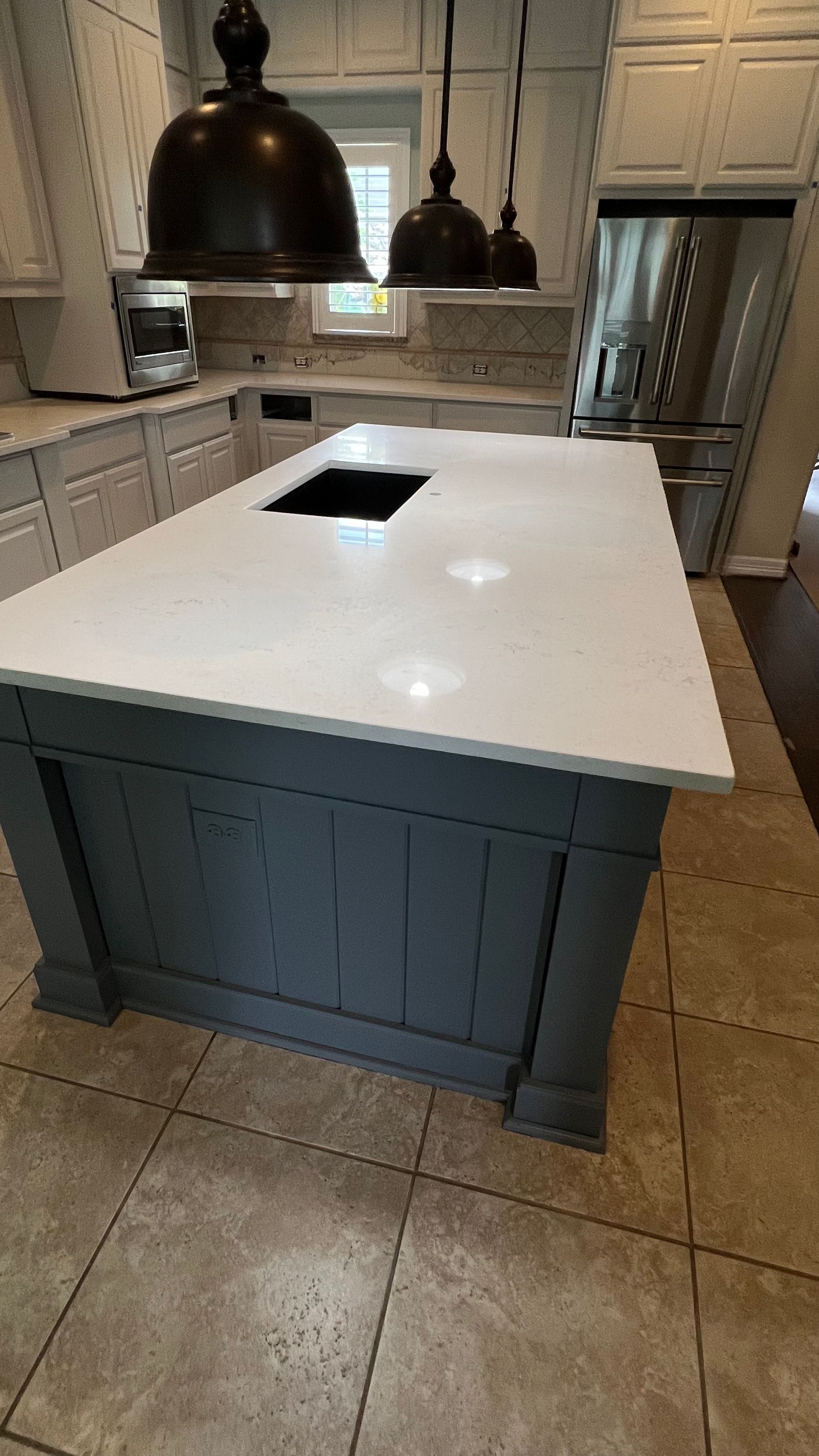 Modern kitchen island with white countertop, dark blue base, and built-in sink under pendant lights.