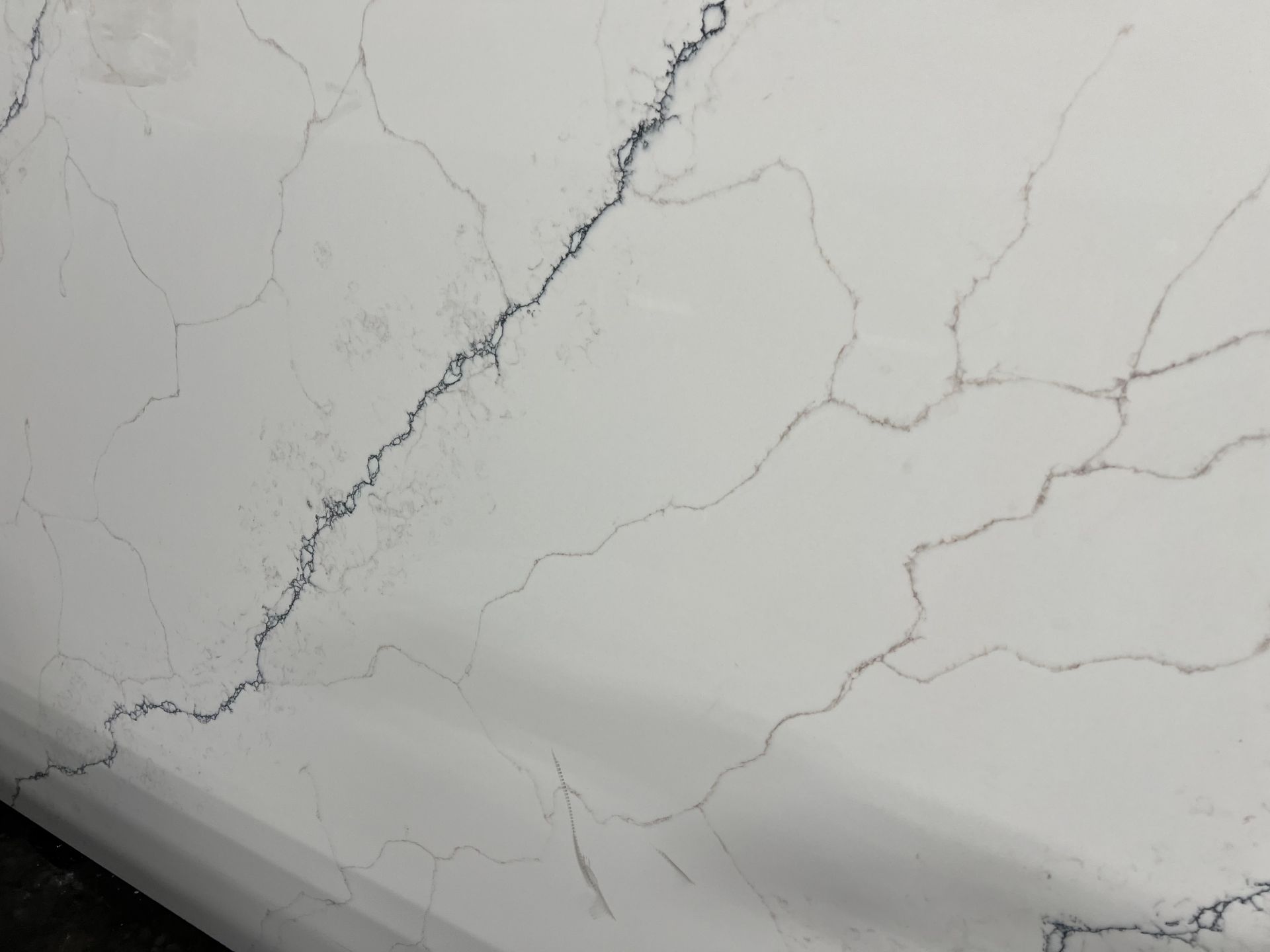 Cracked white marble surface with gray veining and a dark edge at the bottom left