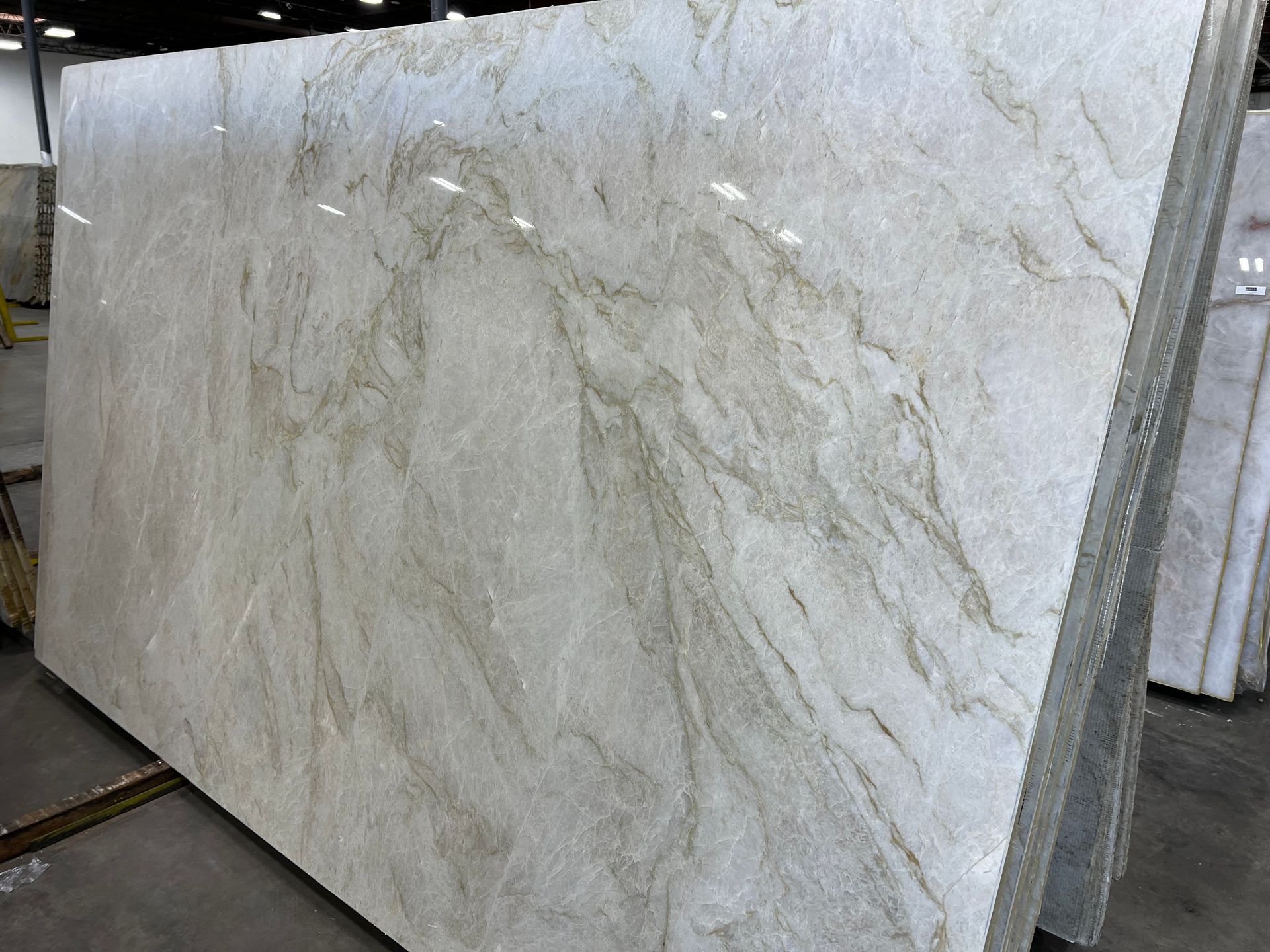 Large polished beige stone slab with light gray veining, displayed upright in a warehouse.