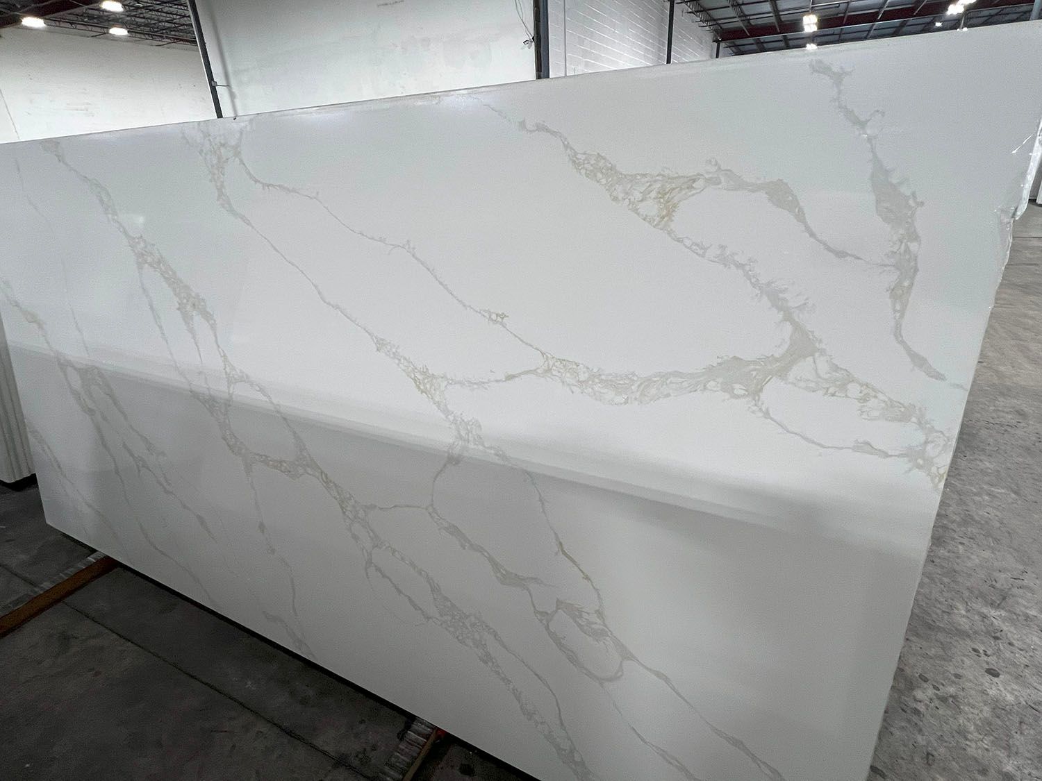 Large white marble-look slab with gray veining, shown upright in a workshop or showroom.
