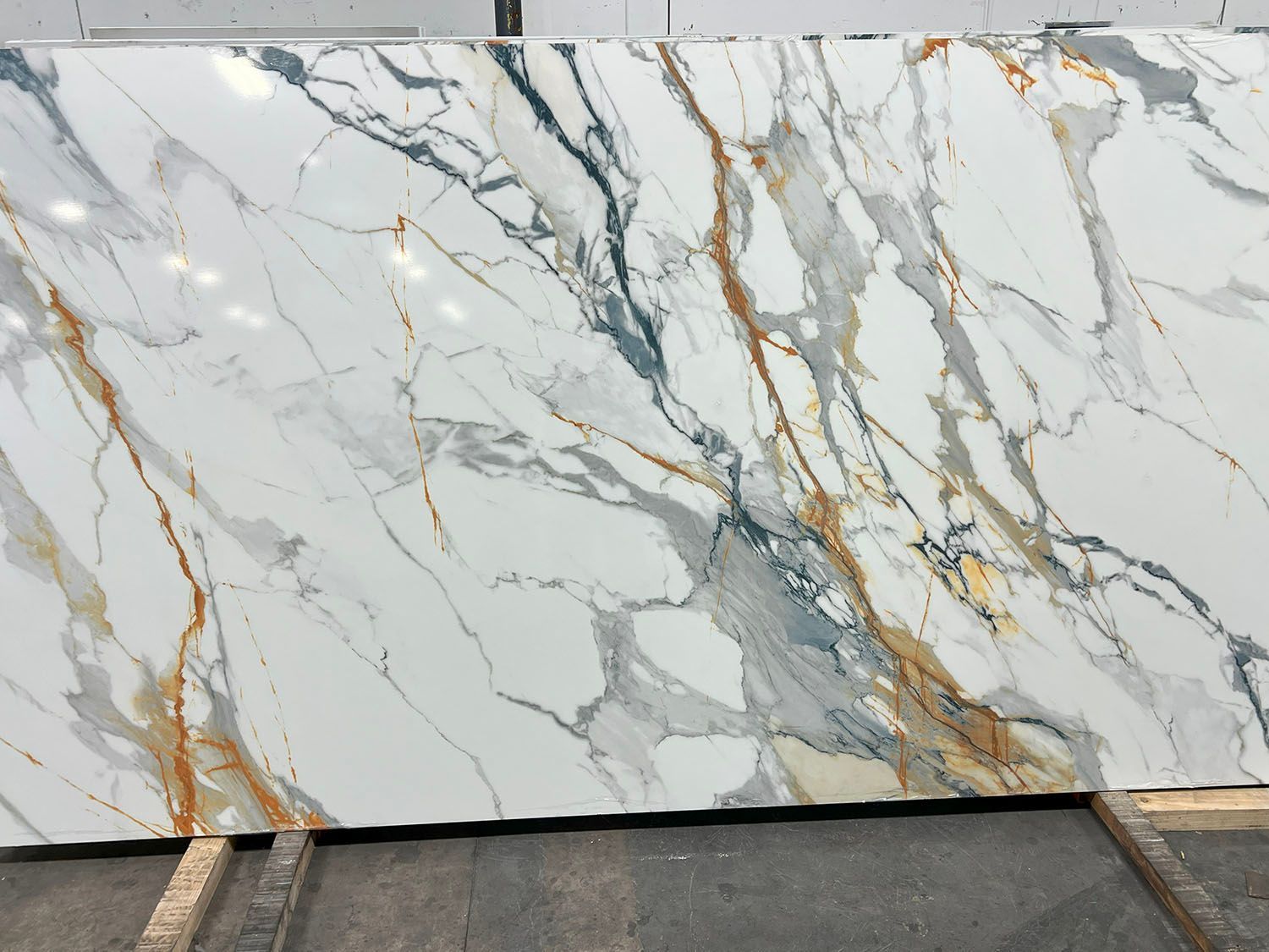 Large white marble slab with gray veining and gold streaks, displayed upright outdoors