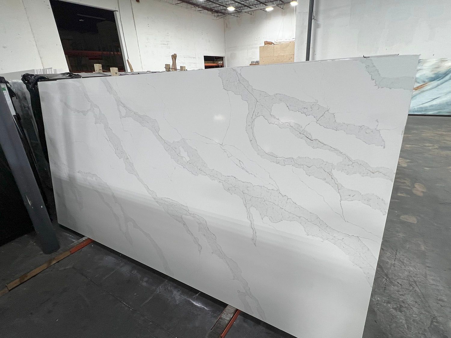 Large white marble-look slab leaning in a warehouse showroom, with faint gray veining and stacked panels nearby