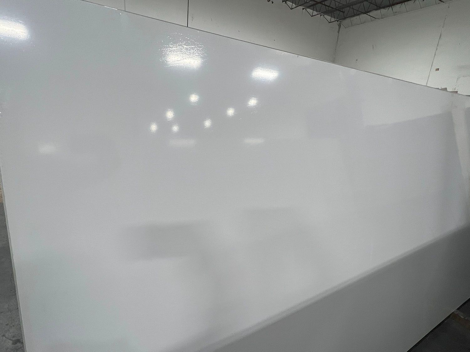 Empty whiteboard in a bright room, reflecting overhead lights.