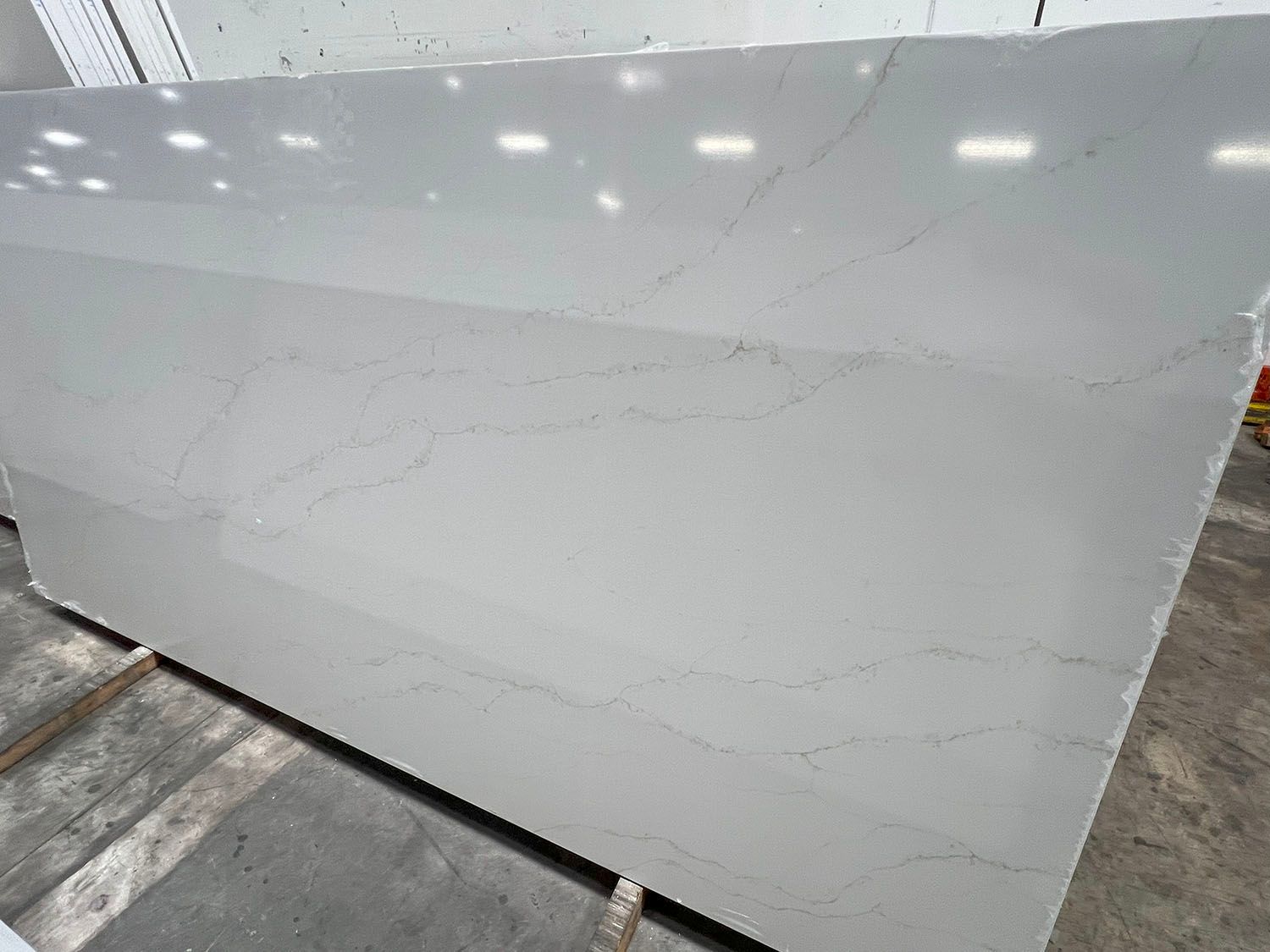 Large white glossy stone slab with subtle gray veining displayed in a warehouse