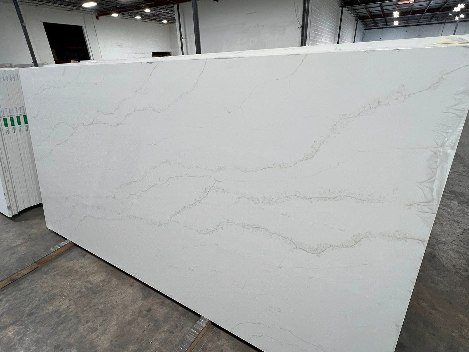 Large white quartz slab with subtle gray veining displayed in a warehouse showroom