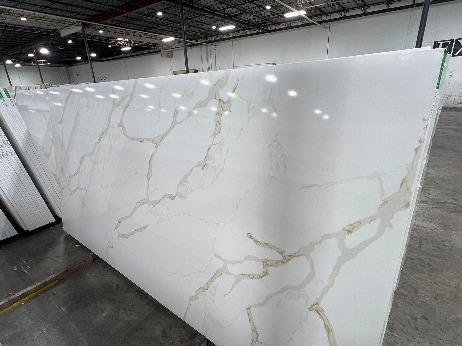 Large white marble-look slab with gold veining displayed in a warehouse showroom