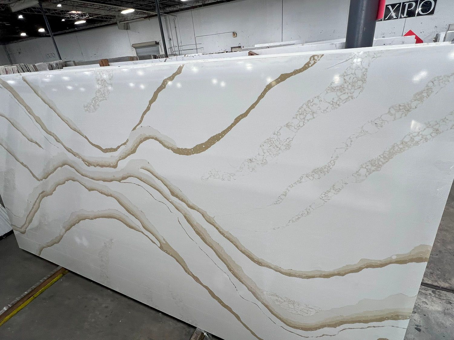 Large white marble slab with gold and gray veining in a warehouse setting