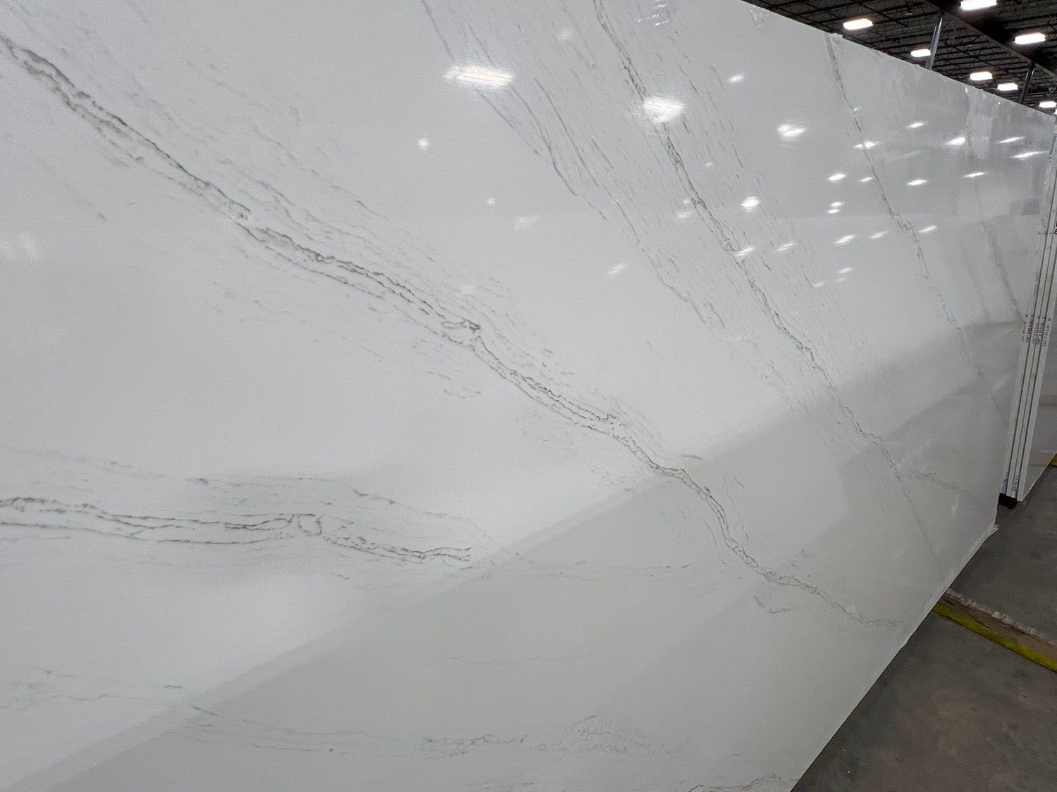 White marble wall panel with gray veins in a bright showroom or warehouse.