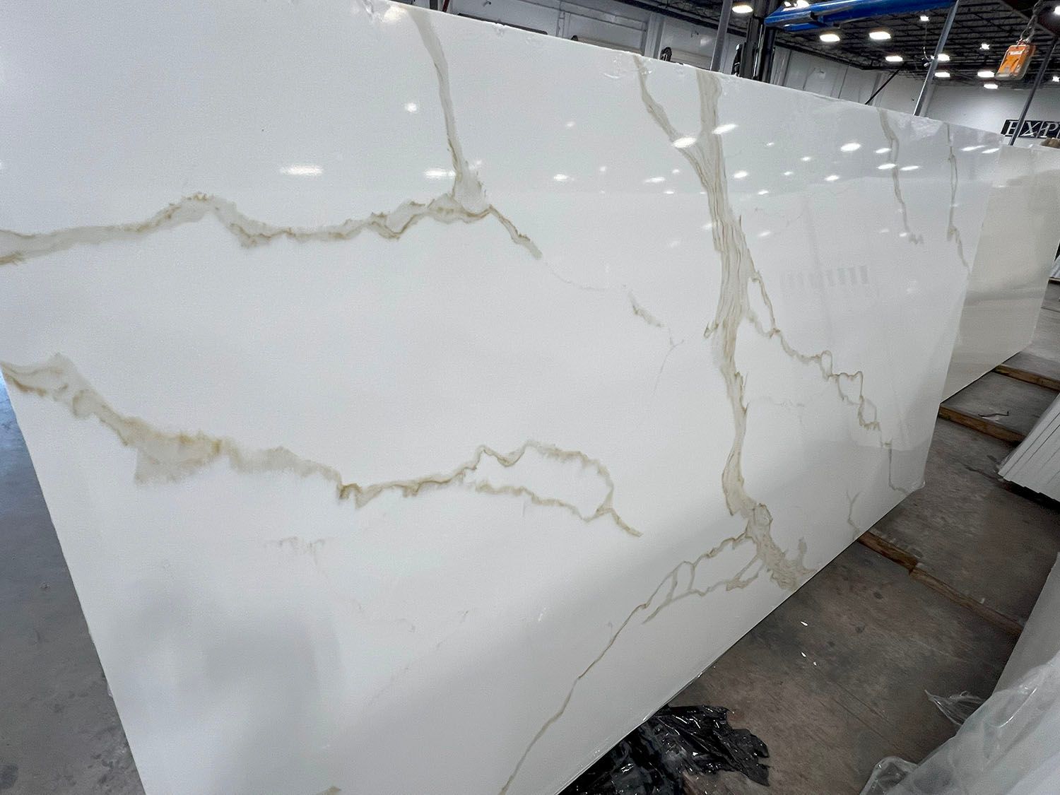 Large white marble slab with gold veining in a workshop, standing upright on the floor
