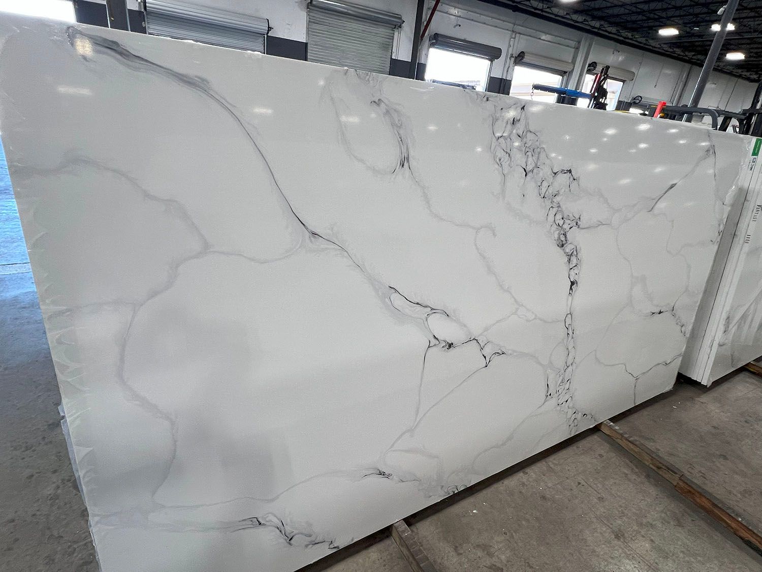 Large white marble-look stone slab with gray veining displayed indoors on a warehouse rack
