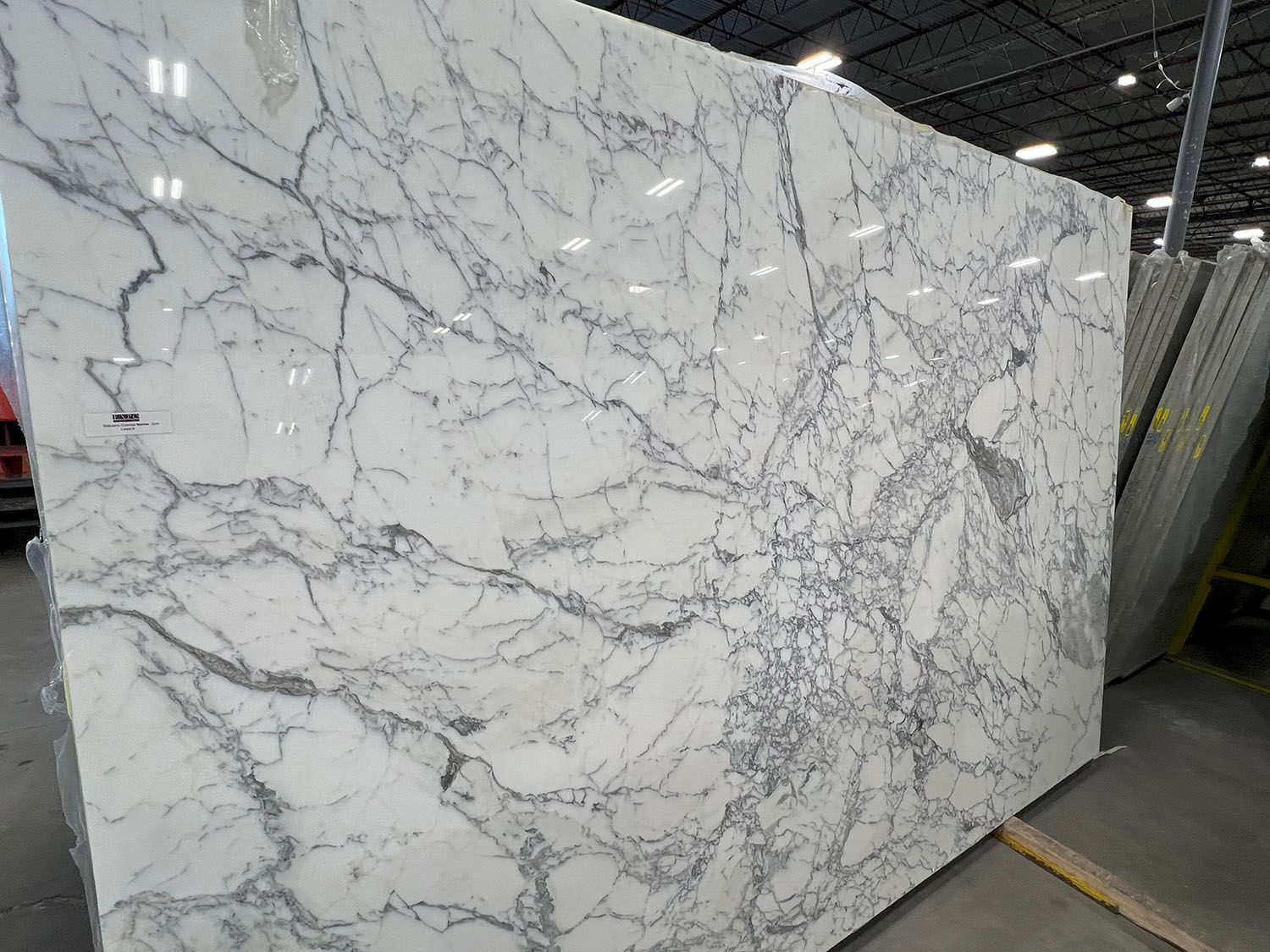 Large white marble slab with gray veining displayed in a warehouse or stone yard