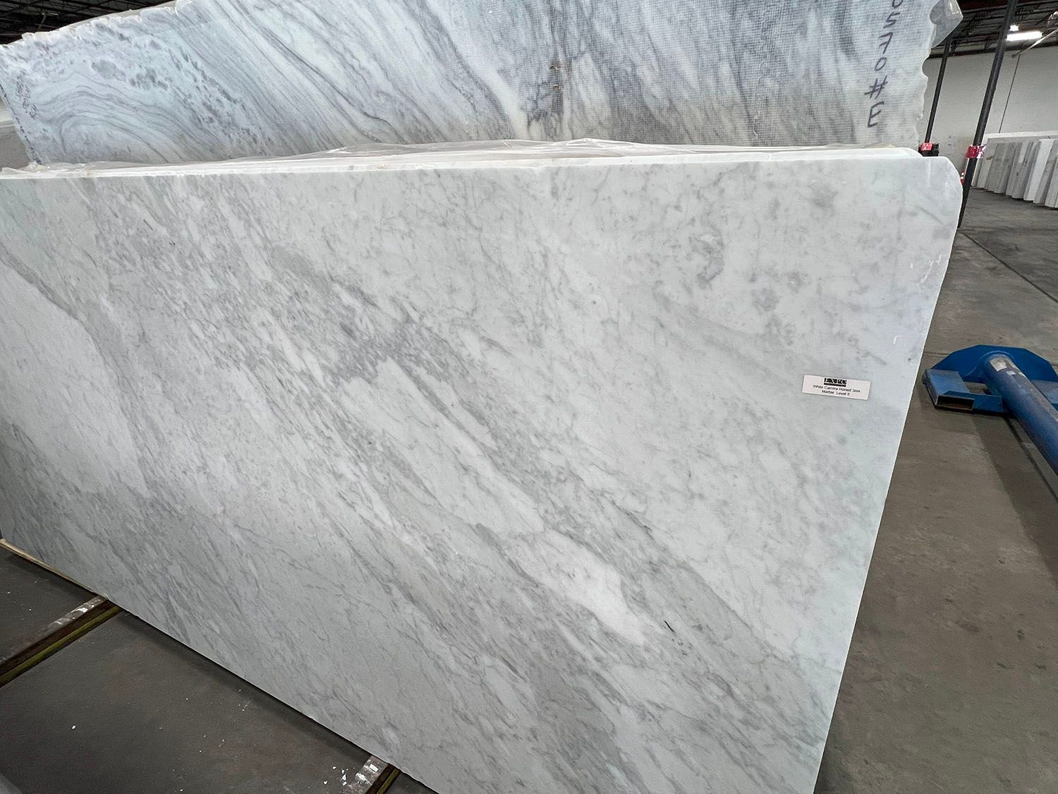 Large white marble slab with gray veining leaning upright in a warehouse or stone yard.