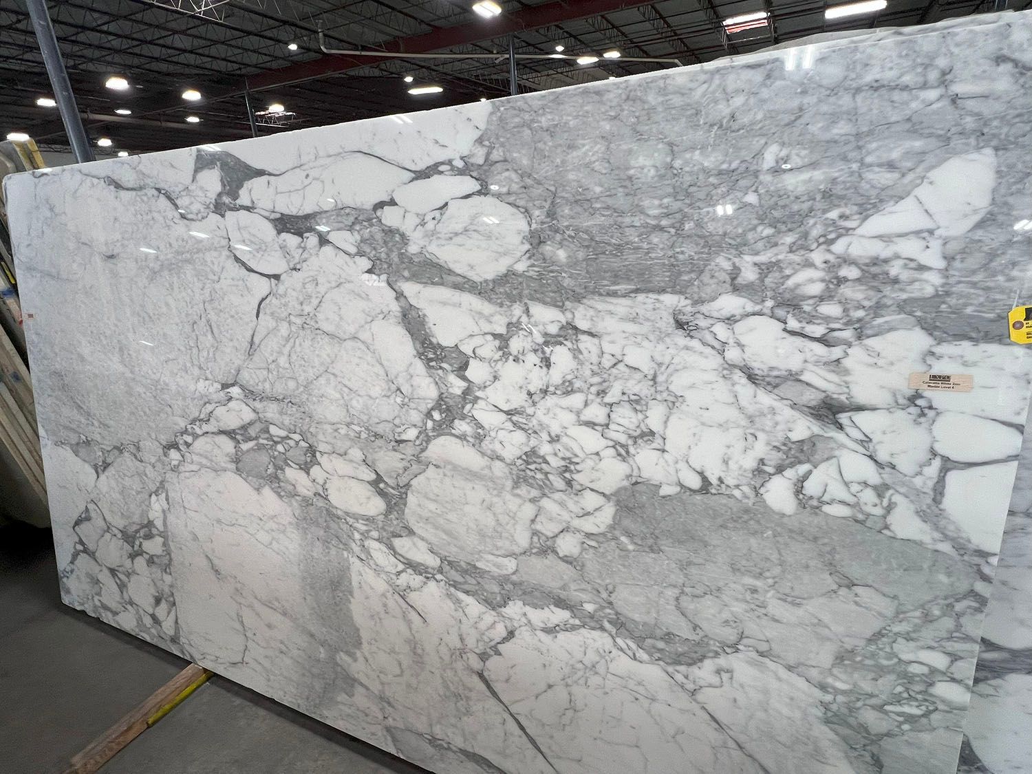 Large white and gray marble slab with bold veining in a warehouse or stone yard