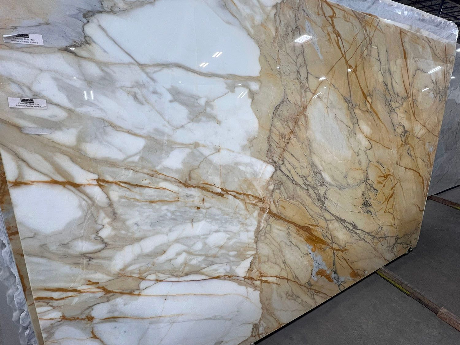 Polished white and beige marble slab with gold veining leaning outdoors
