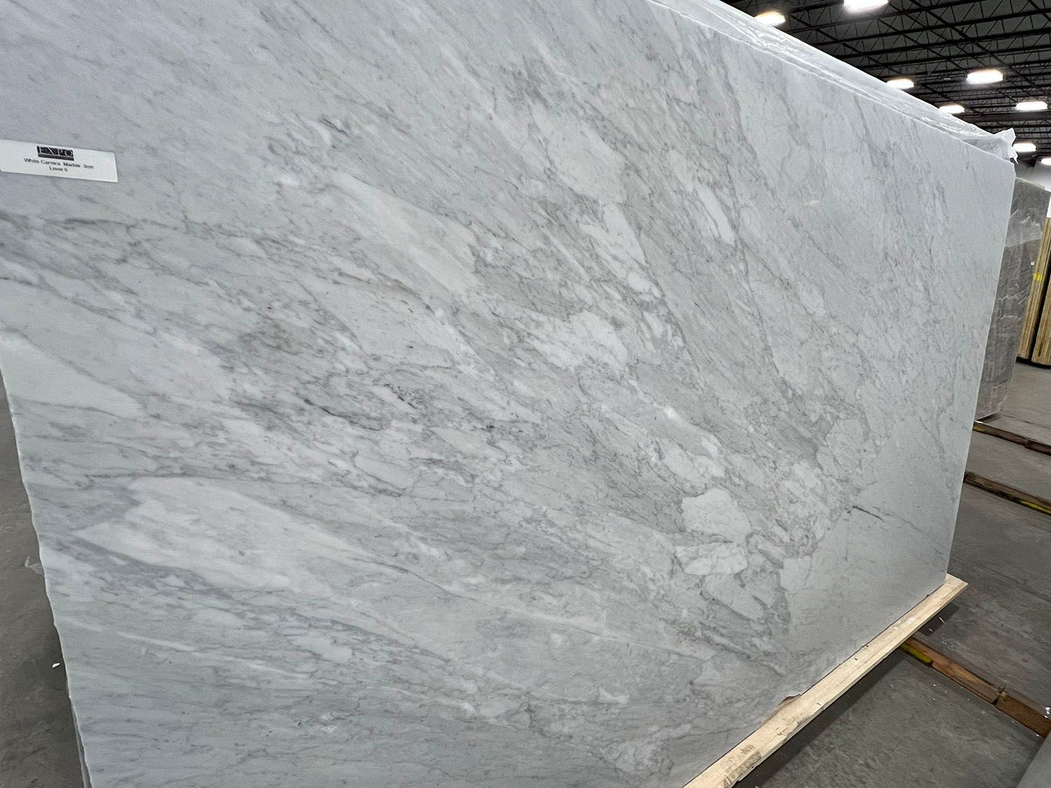 Large gray marble slab with white veining leaning on wooden supports in a warehouse.