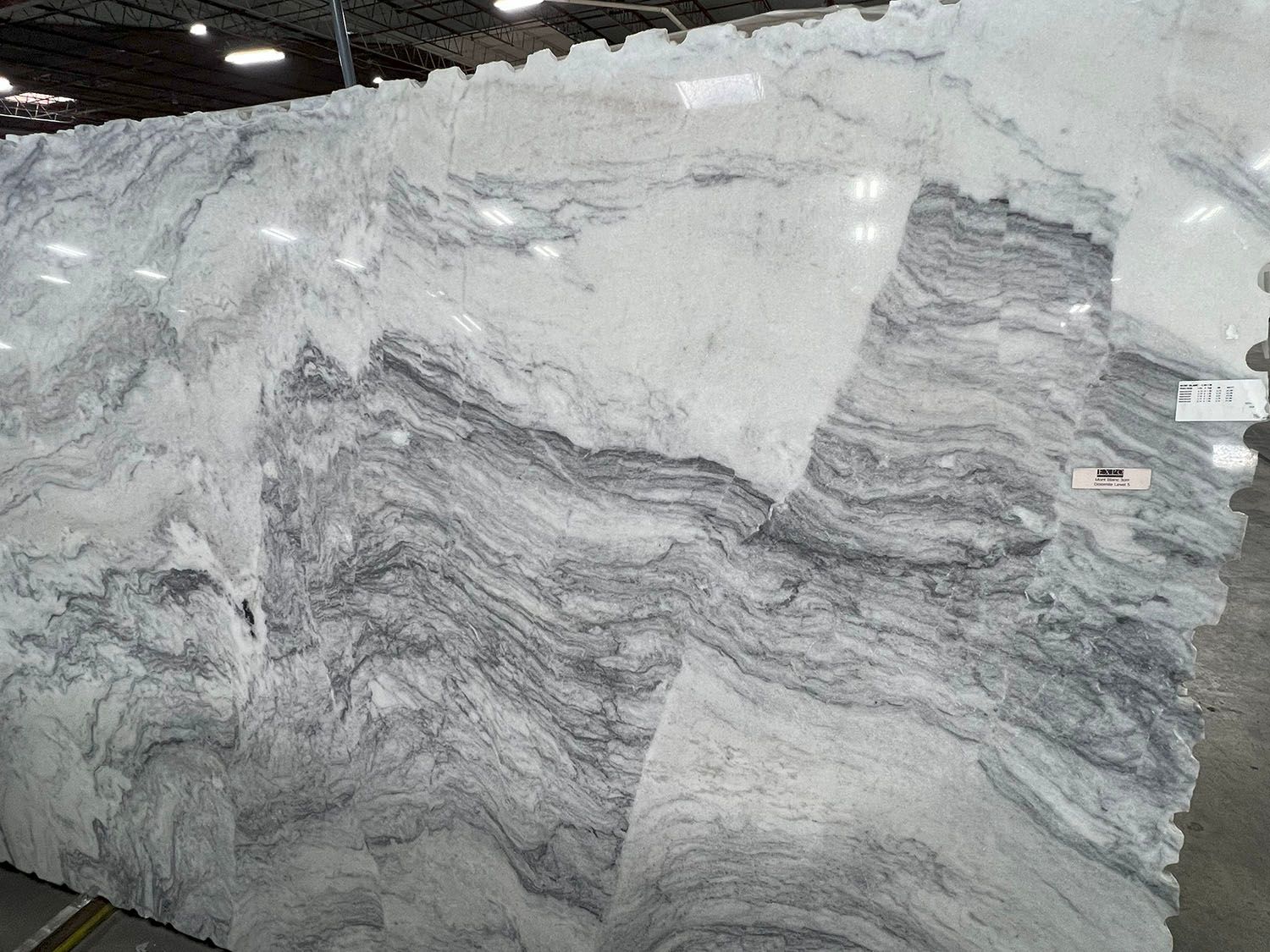Large polished white and gray marble slab with wavy veining in a stone warehouse