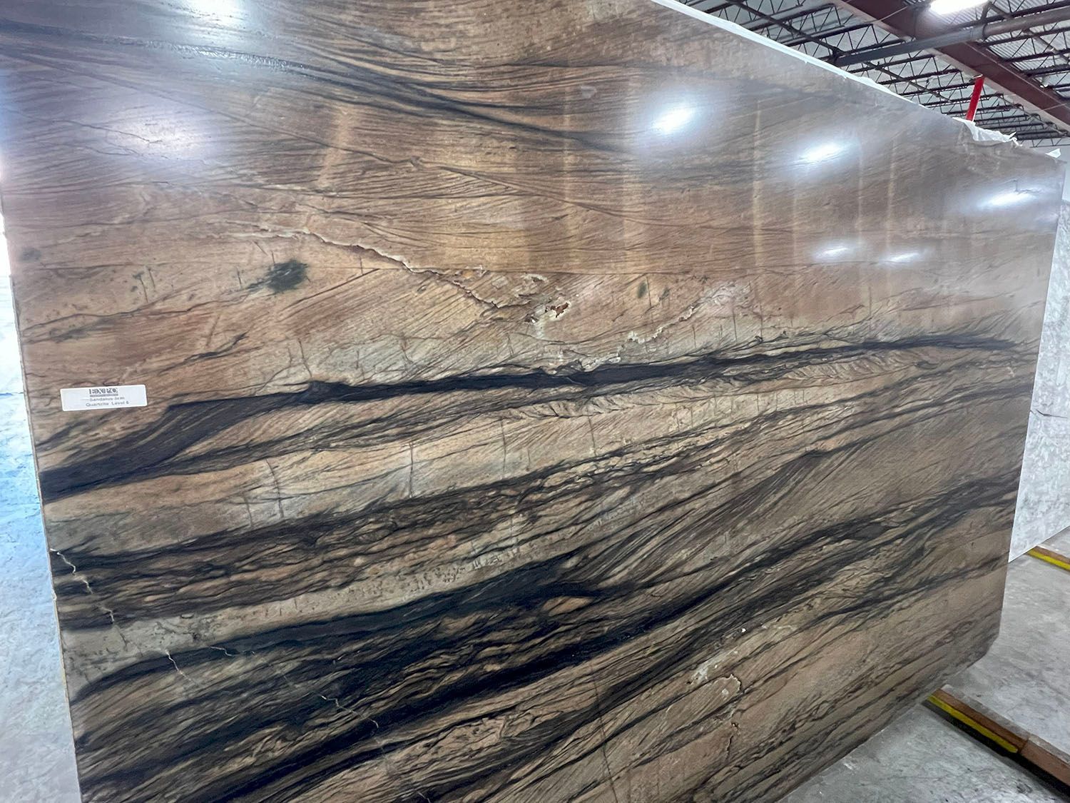 Polished stone slab with brown, cream, and black veining displayed in a showroom
