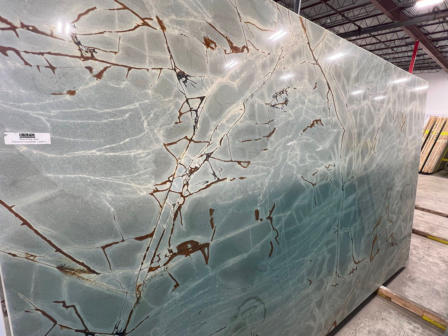 Large polished green-gray marble slab with brown veining in a warehouse or stone yard