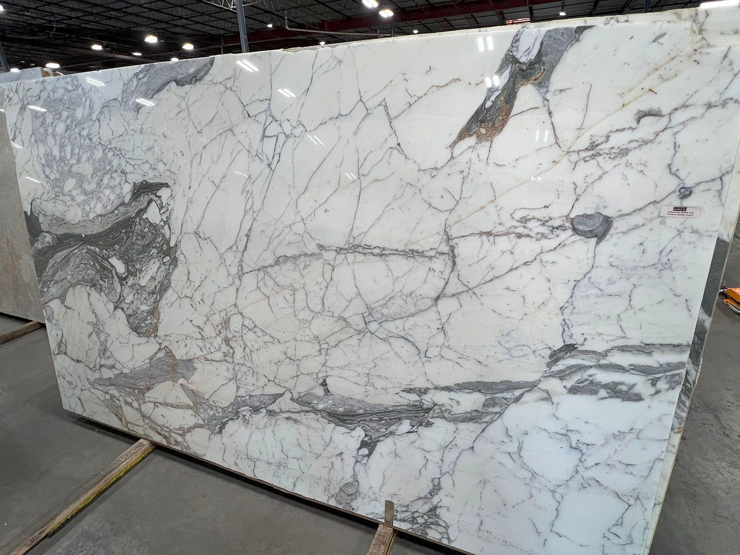 Large white marble slab with gray veining displayed upright on a warehouse floor