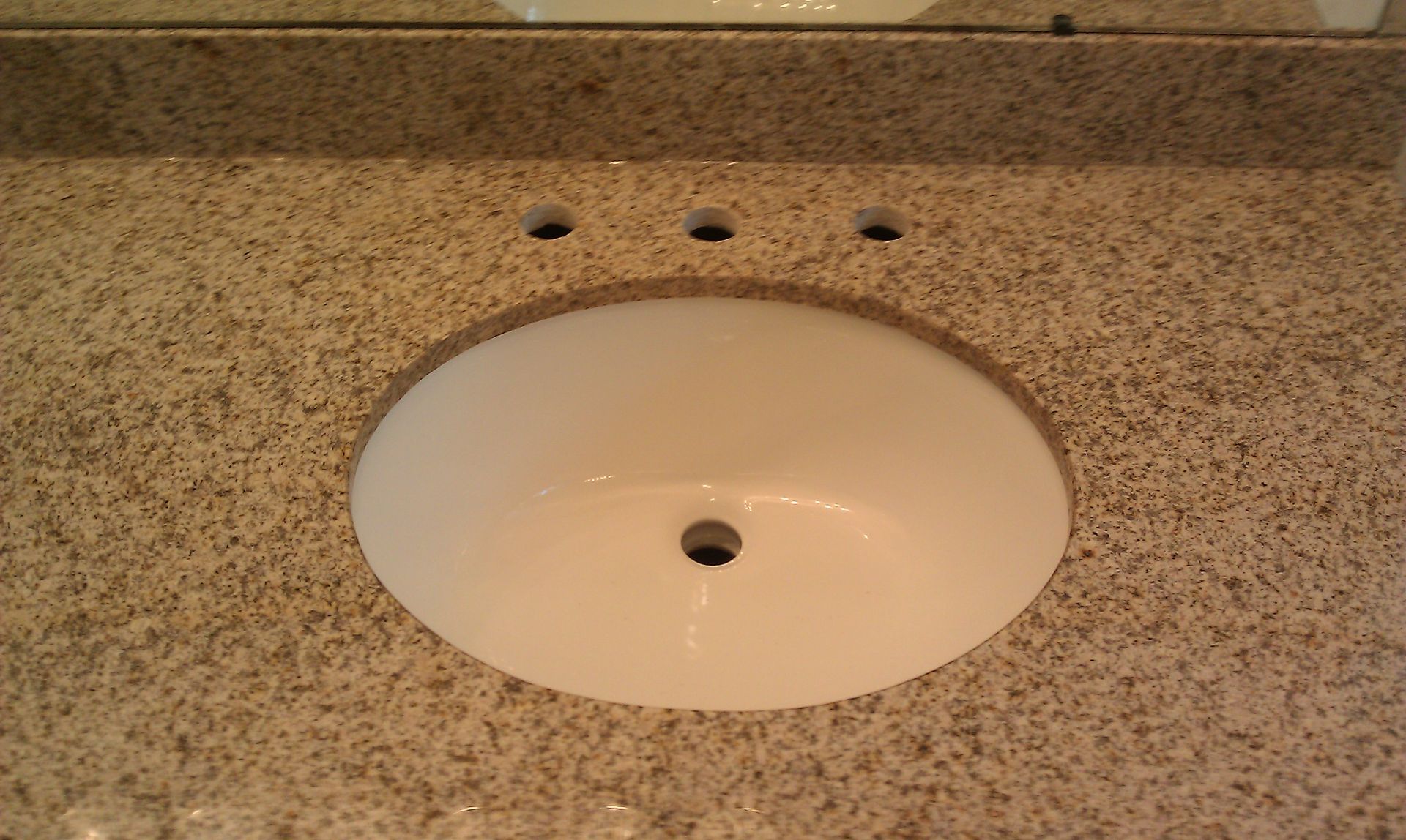 White oval bathroom sink set in speckled granite countertop with three faucet holes above.