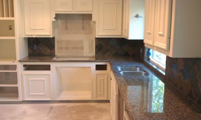 Modern kitchen with white cabinets, granite countertops, tiled backsplash, and a built-in stove area