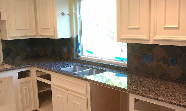 White kitchen with granite counters, cream cabinets, tiled backsplash, and a window above the sink.