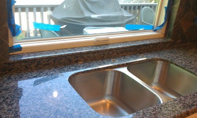 Kitchen counter with stainless steel double sink beneath a window and blue dish rack outside