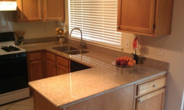Kitchen with wooden cabinets, a countertop, sink under a window, and fruit bowl near the stove.