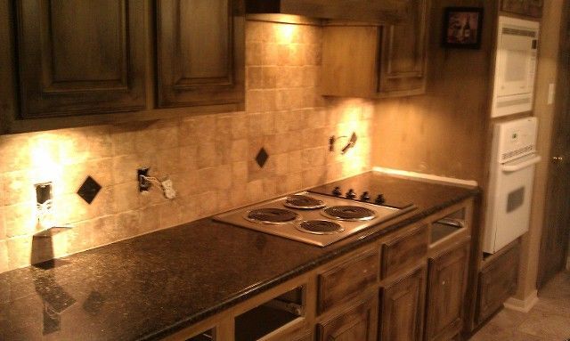 Warm kitchen with wooden cabinets, tiled backsplash, and stainless steel gas stove under under-cabinet lights
