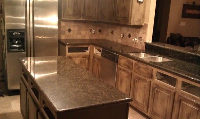 Modern kitchen with granite island, stainless steel fridge, wood cabinets, and black countertops