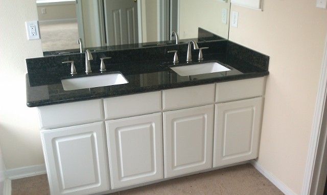 Modern bathroom vanity with black countertop, white cabinets, and two sinks, shown against a beige wall