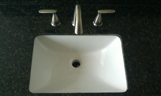 White bathroom sink with chrome faucet and handles on a dark countertop.