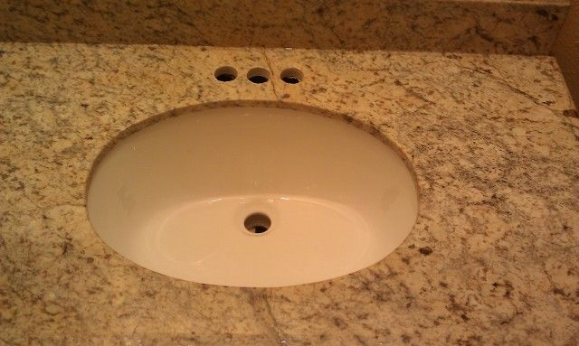 Beige bathroom sink set in speckled granite countertop with faucet holes above it