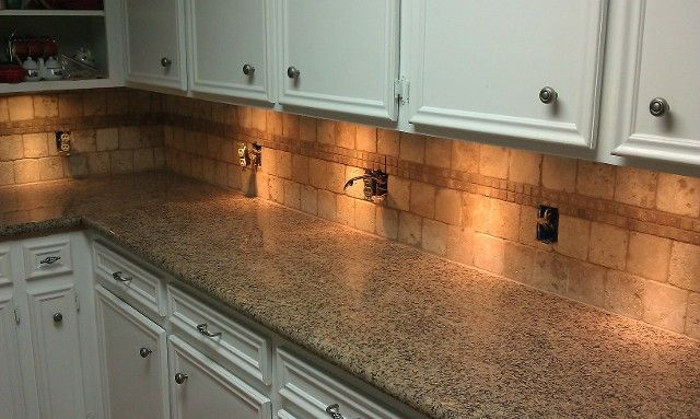 Empty kitchen countertop with white cabinets, granite surface, and warm under-cabinet lighting