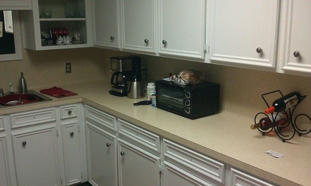 White kitchen countertops with cabinets, coffee maker, toaster oven, and decorative bicycle sculpture.