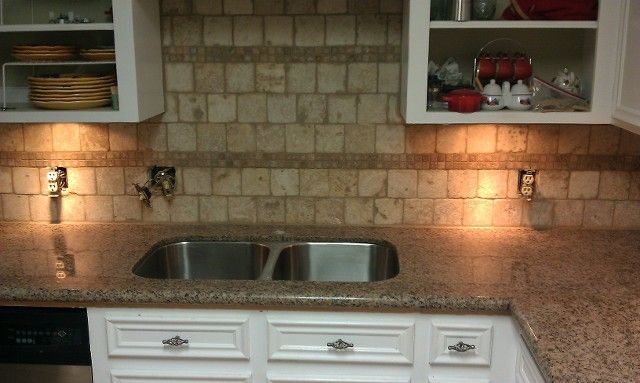 Kitchen sink with granite countertop, white cabinets, open shelves, and warm under-cabinet lighting