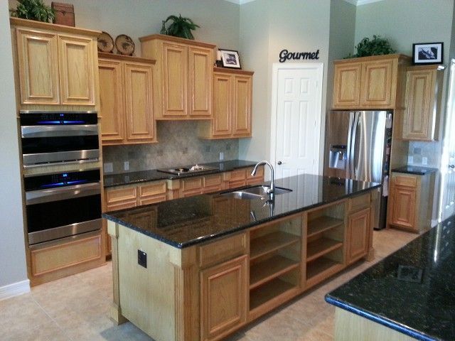 Modern kitchen with wood cabinets, black granite island, stainless steel appliances, and a double oven