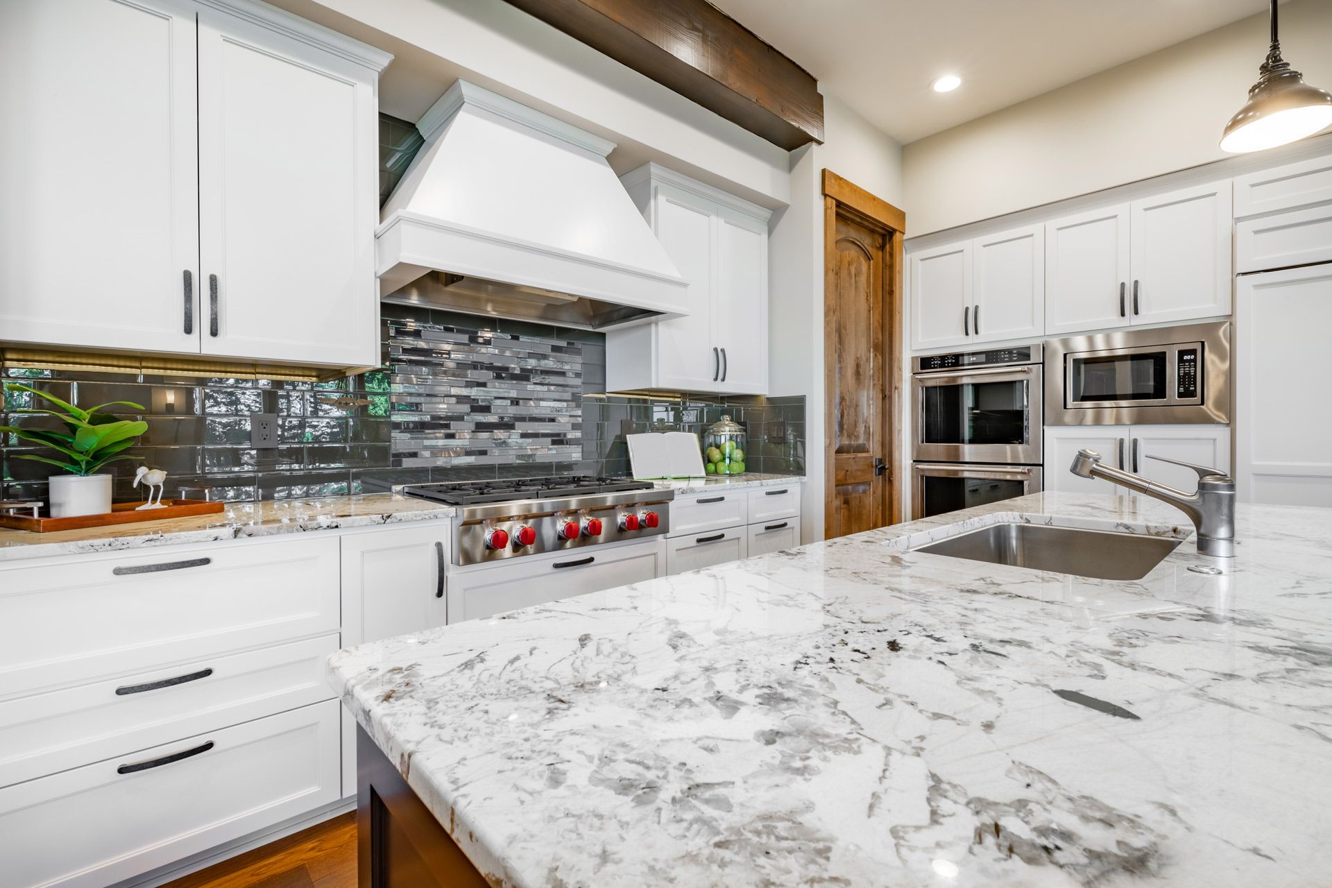 Bright modern kitchen with white cabinets, marble island, stainless appliances, and gray tile backsplash