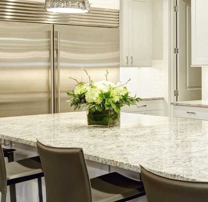 Modern kitchen with stainless-steel fridge, white cabinets, and a granite island with a flower centerpiece